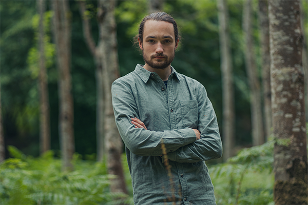 A man stands with his arms crossed in a forest 